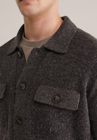 Brun ullskjorta med krage, två framfickor och mörkbruna knappar. Mjuk textur, skräddarsydd passform och subtilt mönster.