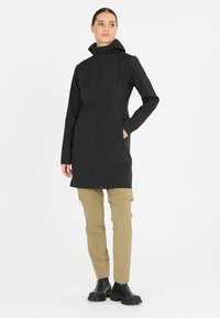 Svart, figurnära jacka med hög krage och dragkedja fram. Kombinerad med beige cargo-byxor och svarta ankelstövlar. Enkelt, stilrent design.
