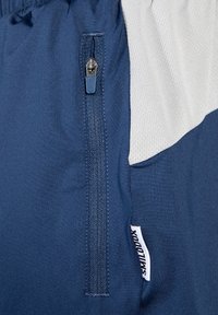 Pantalones cortos deportivos en color azul marino con un bolsillo con cremallera, panel texturizado transpirable en gris claro y una etiqueta de logo posicionada en el lateral.