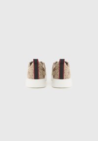 Sneakers i beige tyg med ett diamantmönster, med svarta och röda accenter på hälen och en vit gummisula.