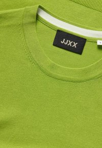 Maglione verde a maglia con scollo rotondo, caratterizzato da una striscia bianca a contrasto sul colletto. L'etichetta mostra il nome del marchio "JJXX" e la taglia "S."