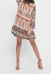 Vestido bohemio de tela ligera con escote en V, mangas largas, patrones geométricos en rojo y azul mezclados, y un dobladillo con volantes en capas.