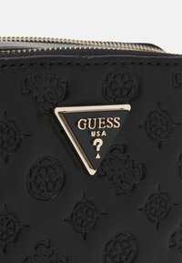 Borsa sintetica nera con superficie texturizzata e motivi in rilievo. Presenta una placca con logo triangolare dorato e una chiusura con zip.