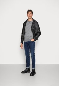 Zwarte leren motorjack over een grijs sweater, gecombineerd met blauwe jeans en zwarte Chelsea boots. Soepele stof en fitted ontwerp.