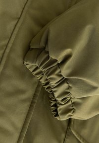 Manche de veste vert olive avec poignet élastique et couture visible sur le tissu rembourré.