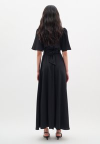 Svart, lång, flödande klänning med korta ärmar, en figurnära bodice och ett ripsband i midjan. Slät textur, inga synliga mönster.
