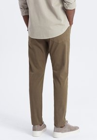 Chinos khaki à coupe slim, avec des poches latérales, des poches arrière et un tissu en mélange de coton lisse. Assortis à des baskets grises claires.