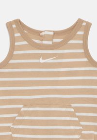 Top sin mangas a rayas en tonos beige y blanco, con escote redondo, un pequeño logo de Nike y un detalle de bolsillo en la parte delantera. Confeccionado en suave material de algodón.