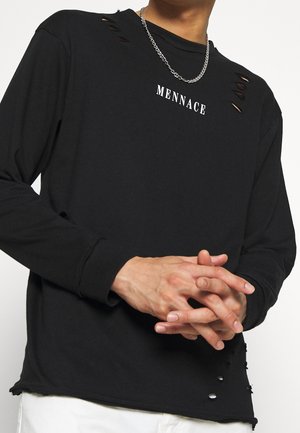 Maglietta nera a maniche lunghe con dettagli a taglio, logo stampato "MENACE" e orlo sfilacciato. Il materiale sembra morbido con una vestibilità comoda.