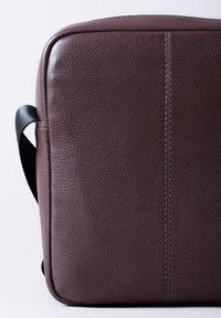 Brown leather briefcase with textured surface, featuring a black strap and visible stitching along the side. Rectangular shape; minimalist design.