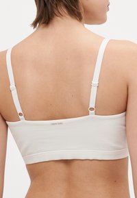 Biely bavlnený bralet s nastaviteľnými ramienkami, hladkou textúrou, bandážovým spodkom a jemným logom na zadnej strane.