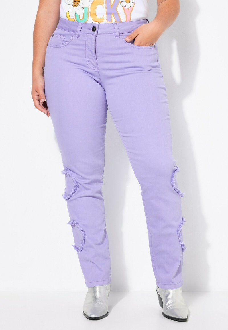 Jeans de mezclilla púrpura con cortes en las rodillas con flecos, que presentan un ajuste slim y un diseño clásico de cinco bolsillos. Combinados con botas plateadas hasta el tobillo.