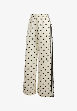 Pantalon blanc à jambes larges avec des pois noirs, taille élastique et bandes Adidas noires avec logo sur le côté.