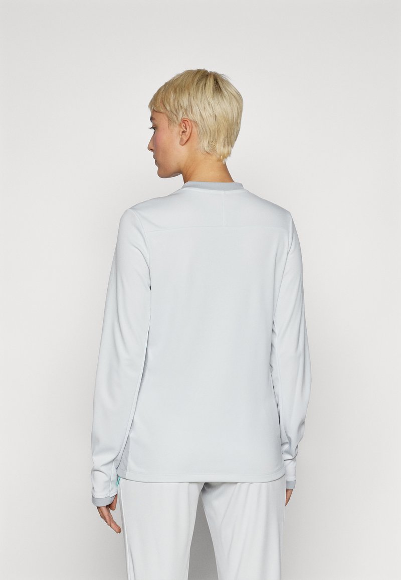 Lange mouw sporttop in lichtgrijs, gemaakt van soepel materiaal, met een ronde kraag en een slank ontwerp met zijkantdetail.