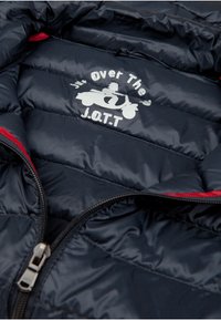 Interno di una giacca puffer blu navy con texture trapuntata, stampa bianca prominente raffigurante uno scooter e testo, e dettagli rossi nella cerniera.