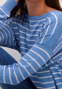 Pull en maille bleu avec des rayures blanches, doté d'un col rond et de manches amples. La texture semble douce et légère.