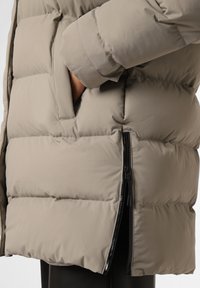 Chaqueta acolchada en tejido gris claro con un diseño acolchado. Presenta bolsillos laterales con cremallera y un ajuste relajado, ideal para climas fríos.