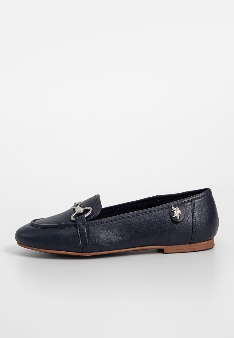 Zapato plano de cuero azul marino con punta redonda, herrajes decorativos de plata y suela de goma marrón. Presenta un detalle cocido en la parte superior.