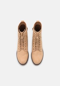 Brązowe botki za kostkę ze sznurowaniem i suwakiem z boku. Wykonane z gładkiej skóry, z zaokrąglonym noskiem i teksturowaną czarną gumową podeszwą.