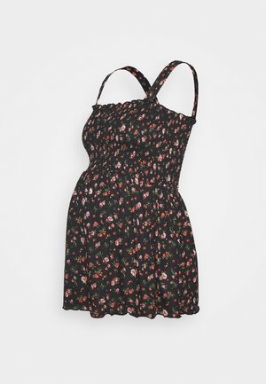 Robe de maternité noire avec motif floral, corsage smocké et bretelles ajustables. Ourlet court avec une forme ample et fluide.