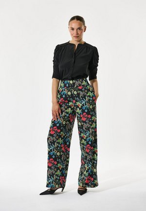 Melna pogaļveida krekls ar pūkainām piedurknēm, kombinēts ar platām biksēm ar daudzkrāsainu ziedu rakstu uz melna fona. Melnas augstpapēžu kurpes.