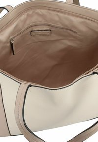 Interior de bolso tote de cuero beige con un bolsillo con cremallera y forro liso. Los bordes tienen un ribete negro y el diseño cuenta con asas dobles.