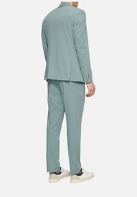 Light blue suit with a structured jacket and straight-leg trousers. Made from smooth fabric, featuring buttons on the jacket's cuffs. Styled with white sneakers.