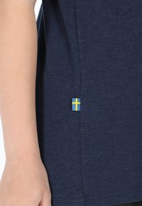 Marineblå bomulds t-shirt med et lille svensk flagtags på siden. Stoffet er blødt, og designet har korte ærmer og rund hals.