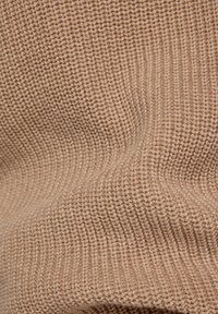 Beiges gestricktes Gewebe mit einem strukturierten, gerippten Muster, das glatte Fasern und einen weichen, flexiblen Fall zeigt. Ideal für Kleidung oder Accessoires.