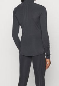 Langärmeliges Sportoberteil aus schwarzem Stretchstoff. Verfügt über einen Stehkragen, nahtloses Design und drei vertikale Linien auf der Rückseite.