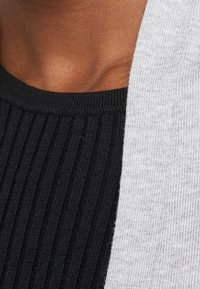 Le tissu noir côtelé à gauche fait une transition vers un tissu gris lisse à droite, créant un design en couches avec des textures contrastées.