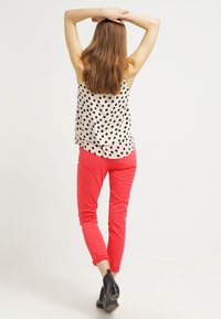 Top senza maniche a pois in crema e nero, abbinato a pantaloni aderenti rosa. La modella è di spalle, mettendo in evidenza il design della parte posteriore dell'outfit.