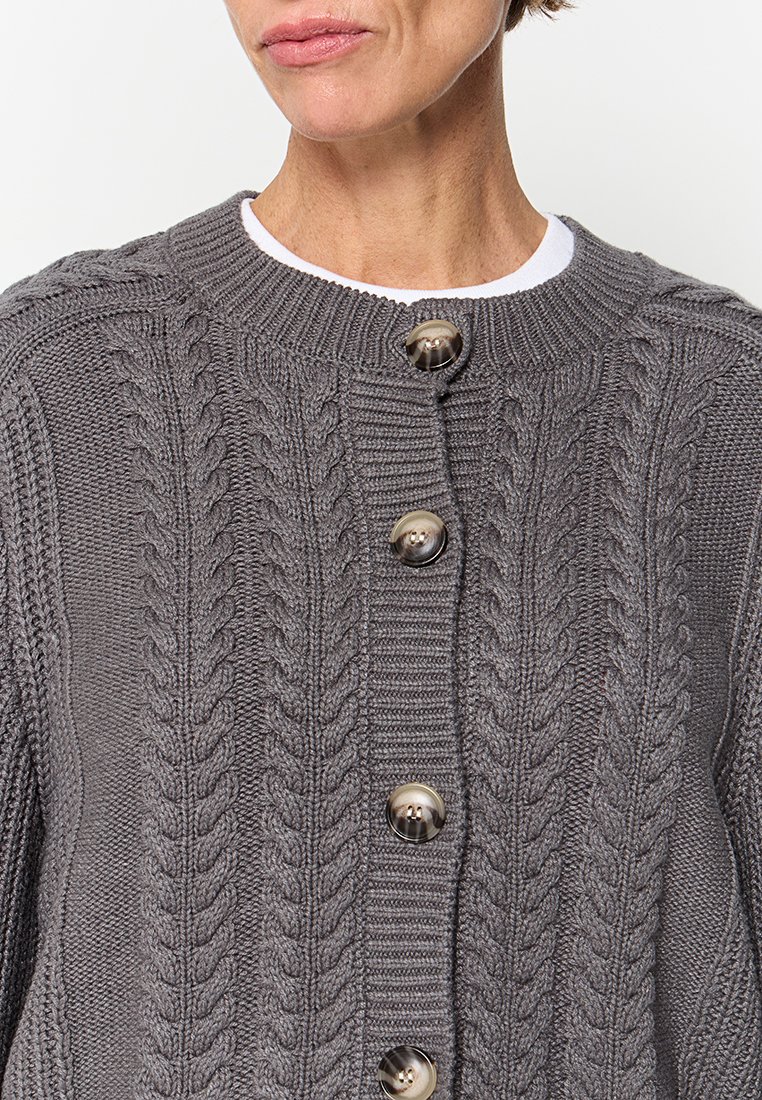 Cardigan en tricot gris avec un motif de câble texturé, présentant un col rond, des coutures visibles et de gros boutons en plastique.