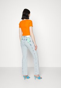 Top laranja com textura em meia manga emparelhado com jeans flare de denim azul claro, apresentando detalhes em verde menta nos bolsos traseiros e saltos turquoise.