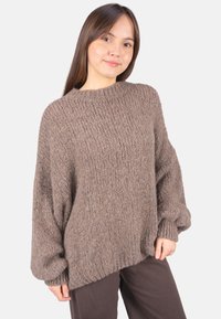 Brauner, grob gestrickter Pullover mit lockerem Sitz, gerippter Textur und übergroßen Ärmeln. Kombiniert mit dunklen, weit geschnittenen Hosen.