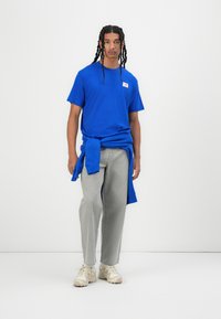 Blåt bomulds T-shirt med et logo-tag, parret med lysegrå løstsiddende bukser og cremede atletiksko, med en sweatshirt bundet om taljen.