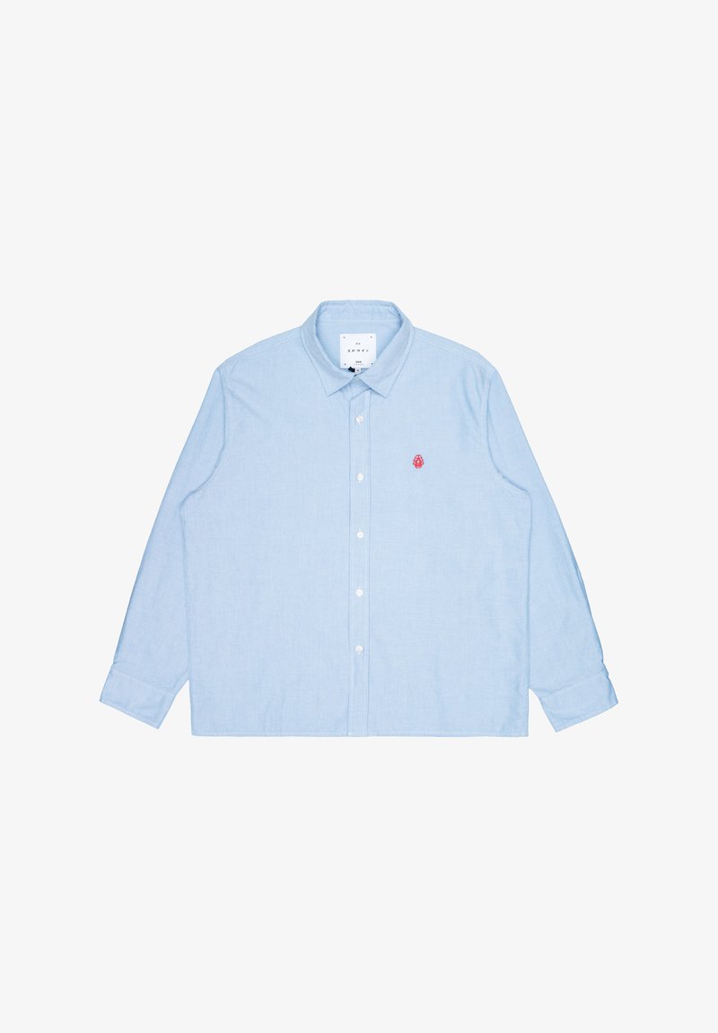 Camisa de manga larga azul claro, hecha de algodón, con cuello abotonado y un pequeño detalle bordado en rojo en el pecho.