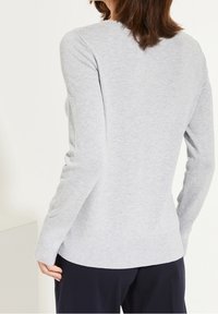 Suéter de color gris claro, con relieve, de manga larga y cuello redondo, que presenta una silueta ajustada y una textura suave.