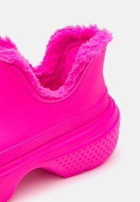 Scarpe sintetiche rosa brillante con rivestimento interno morbido, forma arrotondata, suola testurizzata con fori per la presa e finitura esterna liscia.