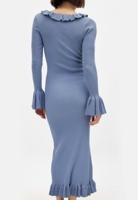 Robe longue à côtes de couleur bleu clair, avec un décolleté à volants et des poignets évasés. Le tissu a une texture lisse et une silhouette ajustée.