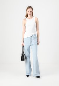 Hvit ermeløs tanktop, lyseblå vide jeans, svart håndveske med strukturert form, og spisse svarte sko på en nøytral bakgrunn.