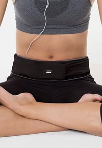 Black fitness belt made of elastic material, featuring a smooth texture and minimal design, worn over a crop top and leggings.