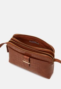Brązowa torebka typu crossbody z teksturowanej skóry, wyposażona w trzy zamykane na zamek kieszenie, złote wykończenia oraz mały zamek z przodu.