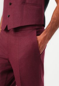 Bordeaux pak met een gestructureerde gilet met drie knopen en broek met een zijzak, gemaakt van een soepel wolmengsel.