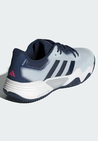 Herrarnas sportig sneakers i vitt och marinblått med svarta ränder, utrustad med dämpad sula och "Solematch"-märke på hälen.