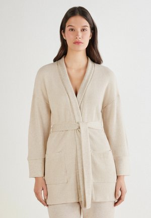 Robe en tricot beige avec un design à enrouler, des manches longues et une ceinture à nouer. Comprend deux poches avant et une finition en tissu texturé.