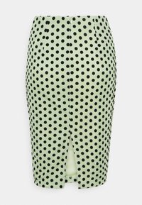 Jupe crayon vert clair à pois noirs, avec une fermeture éclair au dos et une fente centrale dans le dos.