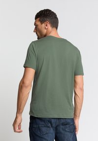 Olijfgroene T-shirt met korte mouwen en een ronde hals, gemaakt van zachte stof, weergegeven vanachter, gecombineerd met blauwe jeans.