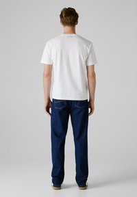 Biała bawełniana koszulka z krótkim rękawem i napisem "PEPE JEANS" z tyłu, w połączeniu z luźnymi, ciemnoniebieskimi dżinsami.