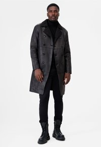 Black leather double-breasted coat with a textured finish, featuring a shearling collar and black buttons, paired with black pants and boots.